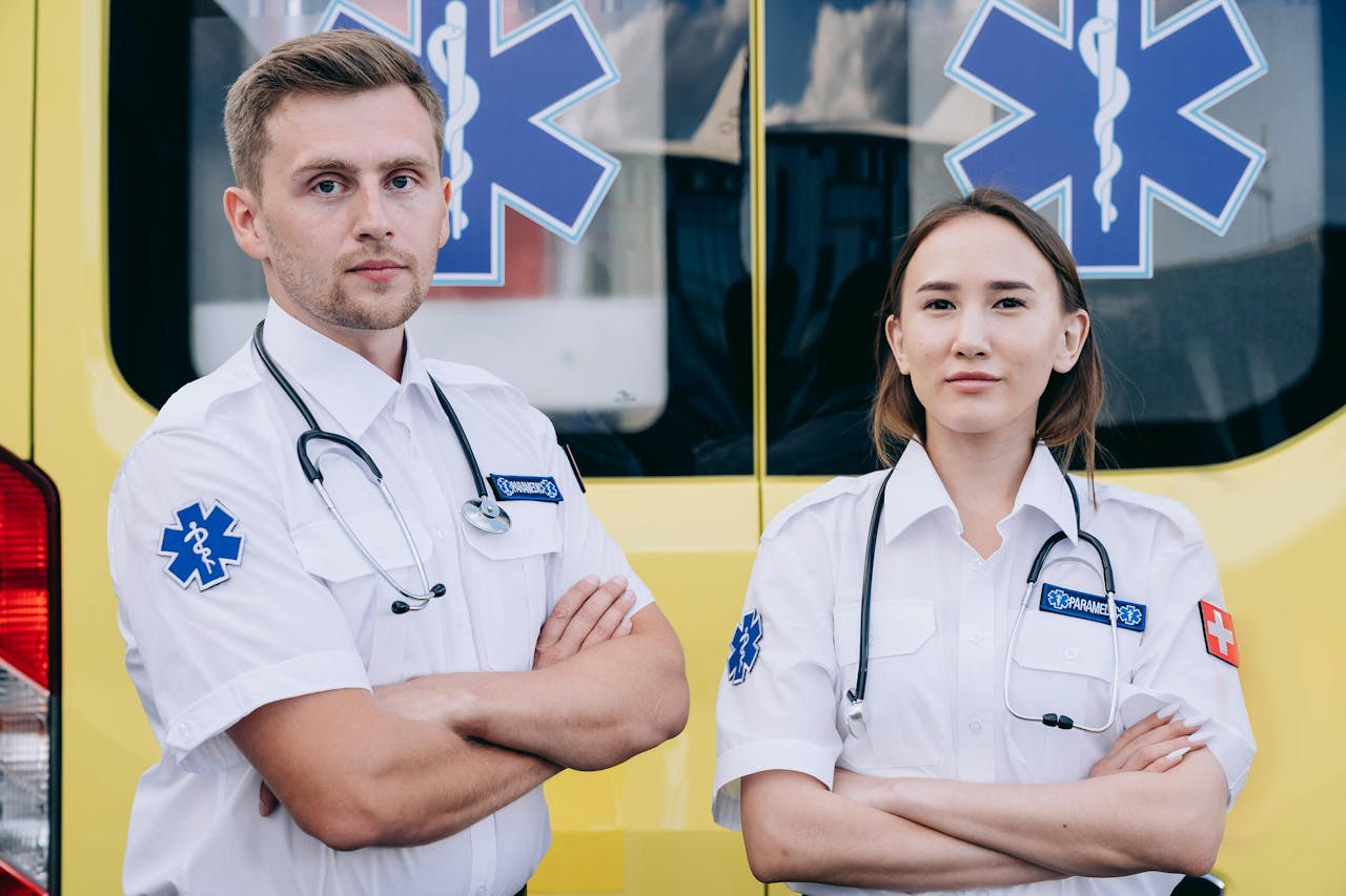 services-01 Portrait of two paramedics with stethoscopes standing confidently in front of an ambulance.
